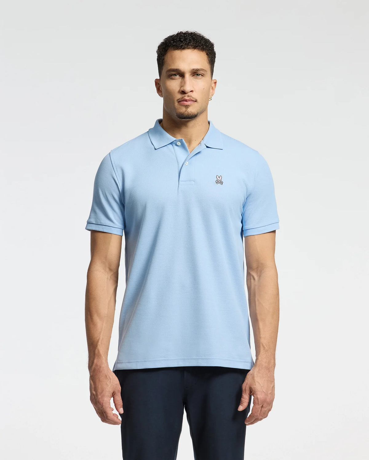 A person wearing the MENS CLASSIC PIQUE POLO SHIRT - B6K001B200 from Psycho Bunny, crafted from soft Pima cotton and featuring a small embroidered Bunny logo on the chest, stands against a plain background.
