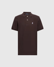 The Men's Classic Piqué Polo Shirt - B6K001D200 by Psycho Bunny is a dark brown polo crafted from soft diamond-knit piqué fabric. It has short sleeves, a collar, and a two-button placket, featuring an embroidered white skull with bunny ears logo on the upper left chest against a light gray background.