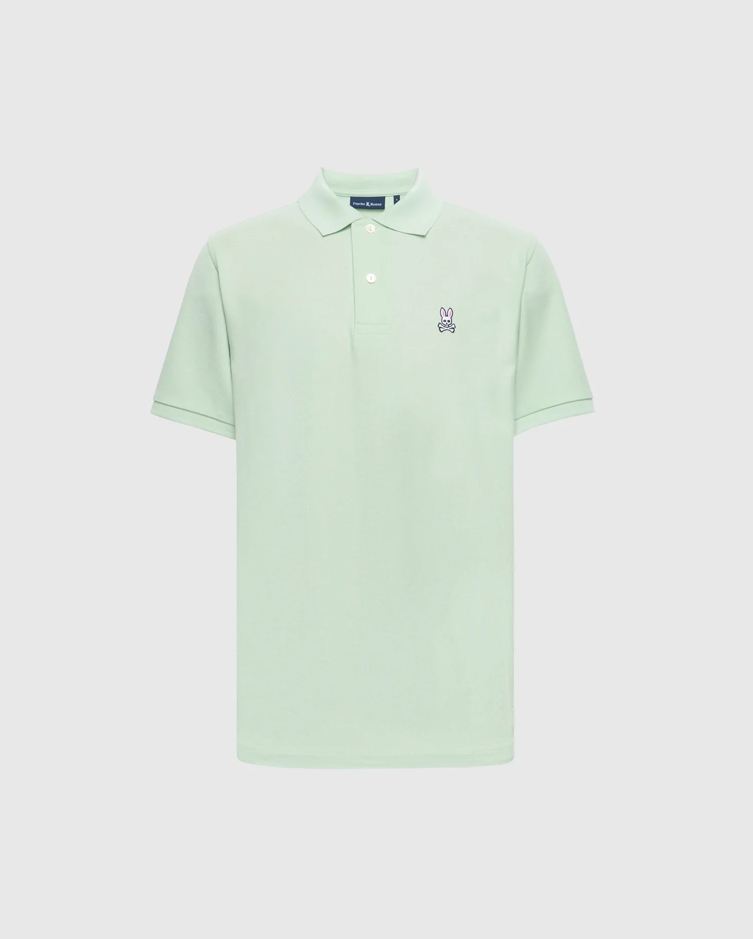 The Psycho Bunny MENS CLASSIC PIQUE POLO - B6K001F200 in light green is crafted from soft Pima cotton, featuring a classic collar, short sleeves, and two white buttons on the placket. It has a small embroidered bunny logo with crossed bones on the left chest against a plain white background.