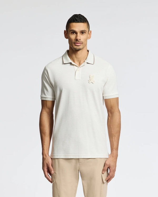 A man models the Psycho Bunny MENS ELDORADO PIQUE POLO - B6K105E200, made of Peruvian Pima cotton with a subtle chest logo. Standing against a white background, he pairs it with regular-fit light khaki pants, arms at his sides, gazing directly at the camera.