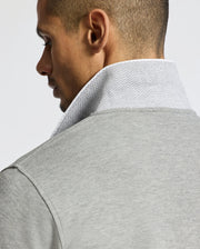 A man is seen from the side and back wearing the Psycho Bunny MENS ELDORADO PIQUE POLO - B6K105E200. This light gray polo, made from luxurious Peruvian Pima cotton, features a subtle zigzag pattern on the collar, highlighting its texture and design.