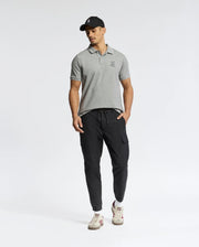 A man wearing a Psycho Bunny Men's Eldorado Pique Polo (B6K105E200), black cargo joggers, white sneakers, and a black cap poses against a plain background.