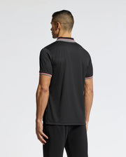 A person with short hair, facing away, wears the Psycho Bunny MENS STRATTON SPORT PIQUE POLO - B6K202E200 in sleek black with red and white trimmed collar and sleeves, paired with black pants. Its moisture-wicking fabric provides comfort against a plain white background.