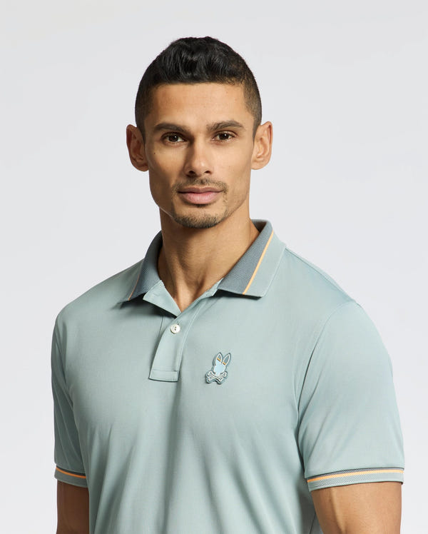 A man in a Psycho Bunny MENS STRATTON SPORT PIQUE POLO - B6K202E200, featuring moisture-wicking technology, confidently faces the camera. His short, dark hair enhances his poised demeanor against a plain light-colored background.