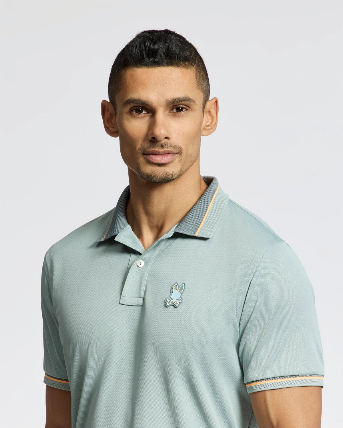 A man in a Psycho Bunny MENS STRATTON SPORT PIQUE POLO - B6K202E200, featuring moisture-wicking technology, confidently faces the camera. His short, dark hair enhances his poised demeanor against a plain light-colored background.