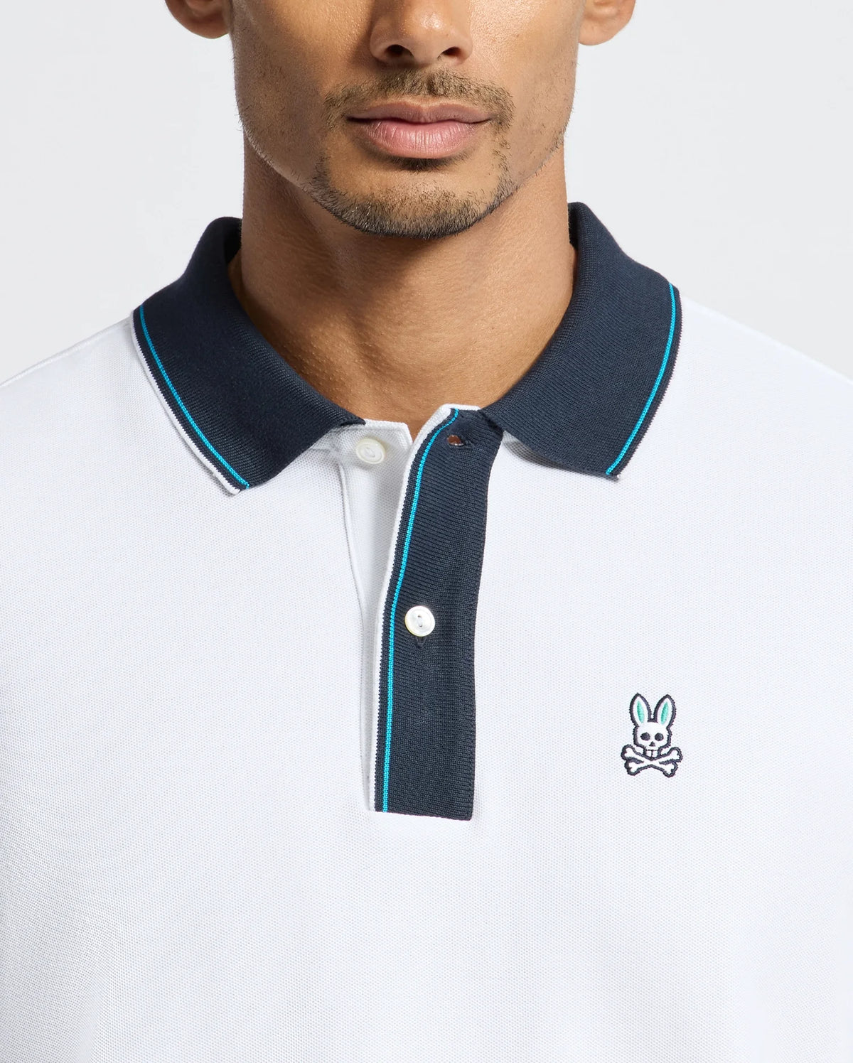 A man wears the exclusive Psycho Bunny MENS BRANDON PIQUE POLO - B6K280E200, distinguished by its black collar and a subtle embroidered rabbit logo on the chest. This luxurious pique polo delivers a modern, casual style ideal for any occasion.