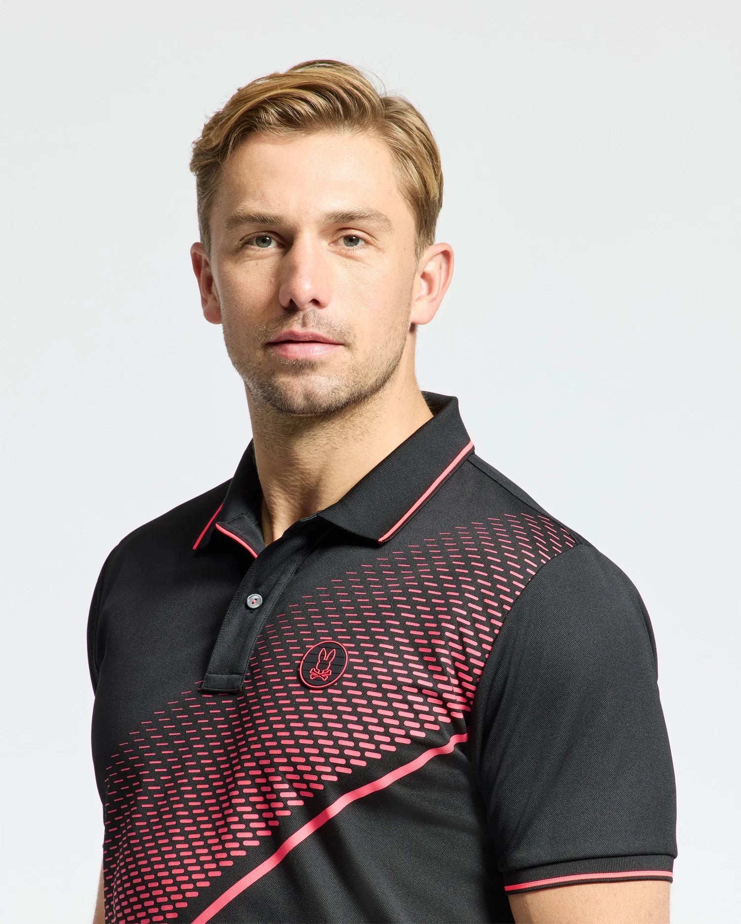 A man in a black and red Psycho Bunny MENS MACK SPORT PIQUE POLO (B6K321E200) with a geometric pattern stands against a plain background, looking at the camera. His short, light brown hair complements this quick-dry shirt, ideal for any occasion.