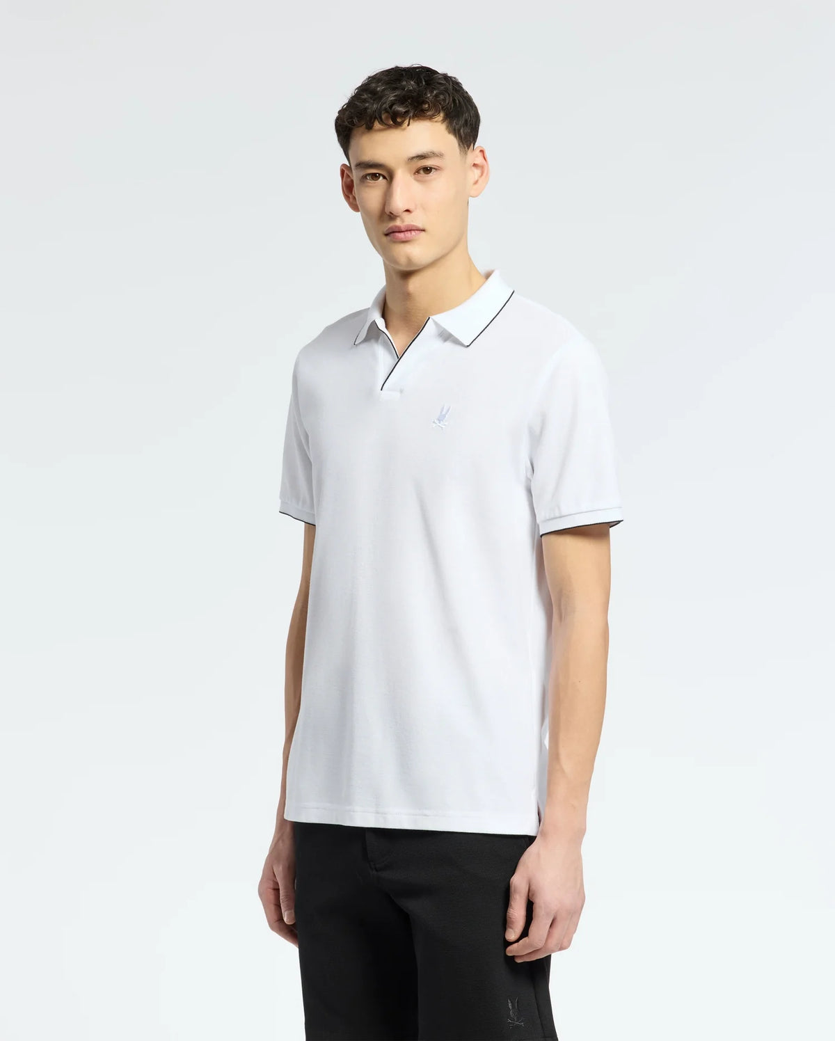 A person in a Psycho Bunny Men's East Hills Johnny Collar Polo, made from soft Pima cotton with black trim, and classic black pants stands against a plain white background.