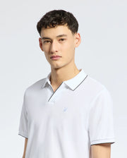 A person with short dark hair is wearing a white Psycho Bunny men's East Hills Johnny Collar Polo (B6K331B200) made from soft Pima cotton, featuring a black trim and small bird logo on the chest. The background is plain white.
