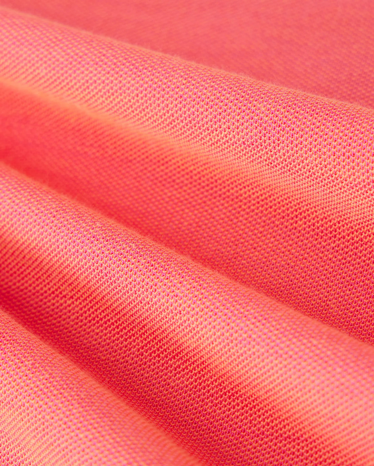Close-up view of folds in a coral-colored Pima cotton-blend fabric showcasing its texture and weave. The MENS WOODWAY OXFORD POLO by Psycho Bunny, adorned with a signature bunny logo, appears smooth with a subtle sheen, while the folds highlight the material's suppleness.