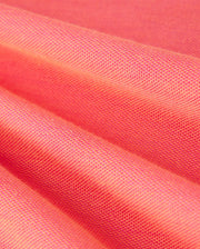 Close-up view of folds in a coral-colored Pima cotton-blend fabric showcasing its texture and weave. The MENS WOODWAY OXFORD POLO by Psycho Bunny, adorned with a signature bunny logo, appears smooth with a subtle sheen, while the folds highlight the material's suppleness.
