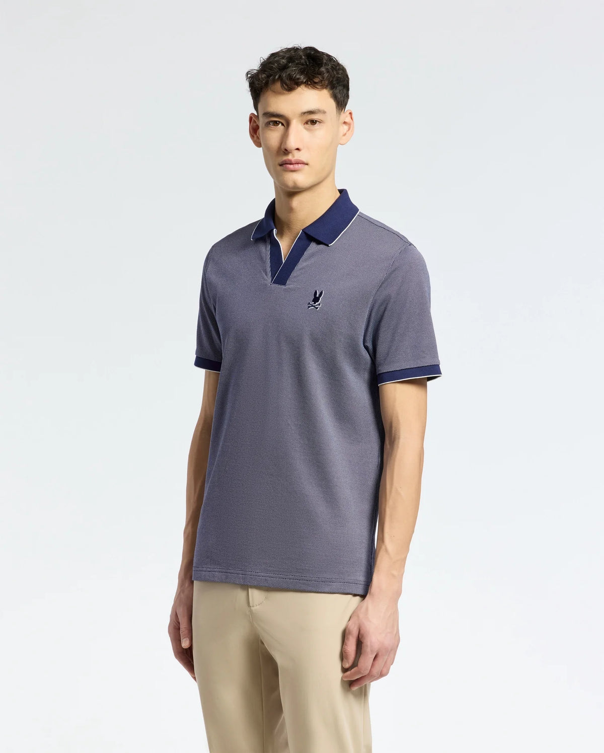 A person models Psycho Bunny's Men's Mackay Jacquard Johnny Collar Polo, B6K408F200, in light navy Pima cotton with a chest emblem and dark navy collar and sleeve edges, paired with beige pants against a plain backdrop.