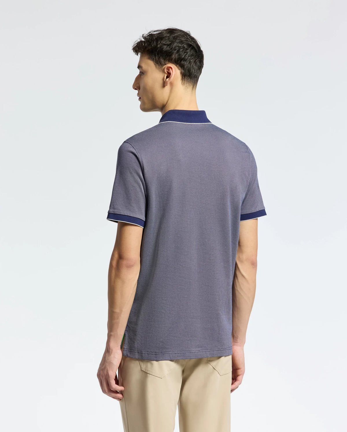 A man with short hair faces away from the camera wearing Psycho Bunny's MENS MACKAY JACQUARD JOHNNY COLLAR POLO in gray with dark blue trim, paired with beige pants, all against a plain white background. Crafted from luxurious Pima Cotton.