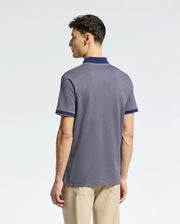 A man with short hair faces away from the camera wearing Psycho Bunny's MENS MACKAY JACQUARD JOHNNY COLLAR POLO in gray with dark blue trim, paired with beige pants, all against a plain white background. Crafted from luxurious Pima Cotton.