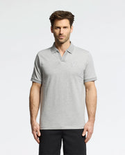 A man in a Psycho Bunny MENS MACKAY JACQUARD JOHNNY COLLAR POLO - B6K408F200, crafted from Pima cotton in light gray with a chest logo, stands against a white background. The polo pairs well with his dark pants. He has short brown hair and a neutral expression.