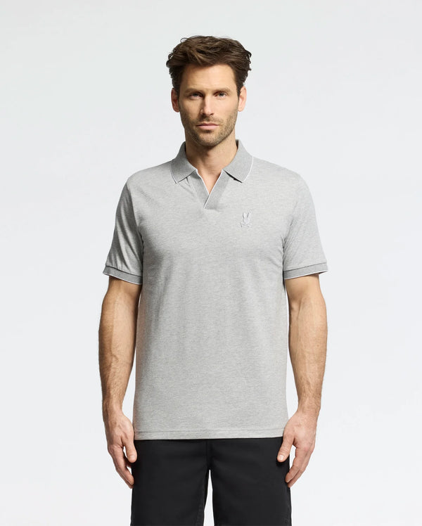 A man in a Psycho Bunny MENS MACKAY JACQUARD JOHNNY COLLAR POLO - B6K408F200, crafted from Pima cotton in light gray with a chest logo, stands against a white background. The polo pairs well with his dark pants. He has short brown hair and a neutral expression.
