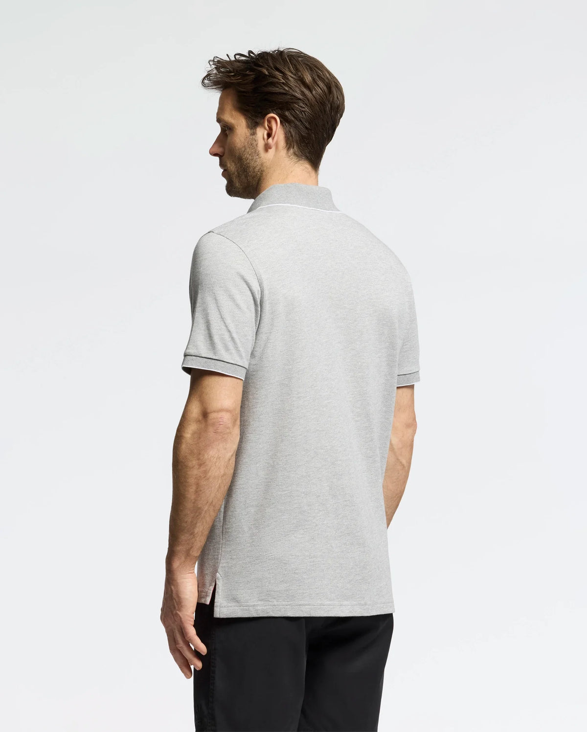 A man with short hair, facing away, dons a Psycho Bunny MENS MACKAY JACQUARD JOHNNY COLLAR POLO - B6K408F200 in gray crafted from pima cotton and pairs it with black pants against a white background.