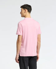 A person facing away from the camera is wearing a light pink Psycho Bunny MENS BRYCE PERFORMANCE PIQUE POLO (B6K486F200) and black pants. The plain light gray background highlights the sophistication of this moisture-wicking attire, perfect for active days.