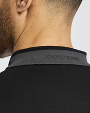 Close-up of the back of a person’s neck in a Psycho Bunny slim-fit black MENS NEW CASTLE PIQUE POLO, B6K487F200. "PSYCHO BUNNY" is subtly embossed on the gray collar. Crafted from soft Pima cotton, it features a sleek plain gray background.