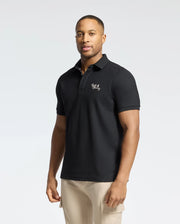 A man showcases timeless style in a Psycho Bunny MENS DESERT PIQUE POLO - B6K506F200, made from luxurious Pima cotton with chest embroidery, paired with khaki pants, set against a plain light gray background.