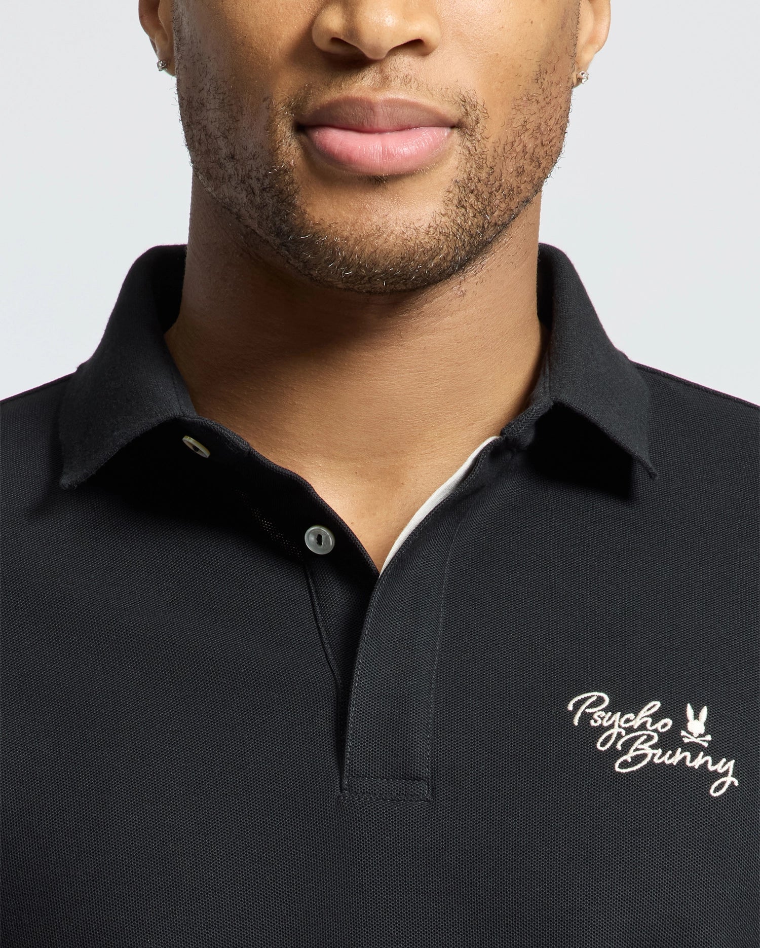 Wearing the MENS DESERT PIQUE POLO by Psycho Bunny, a person exudes timeless style with its embroidered logo on the chest, made from luxurious Pima cotton.