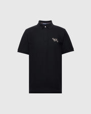 The Psycho Bunny MENS DESERT PIQUE POLO - B6K506F200 in black features a classic collar, two-button neckline, and white embroidered text on the left chest. Made from premium Pima cotton, it offers comfort and timeless style against a light gray backdrop.