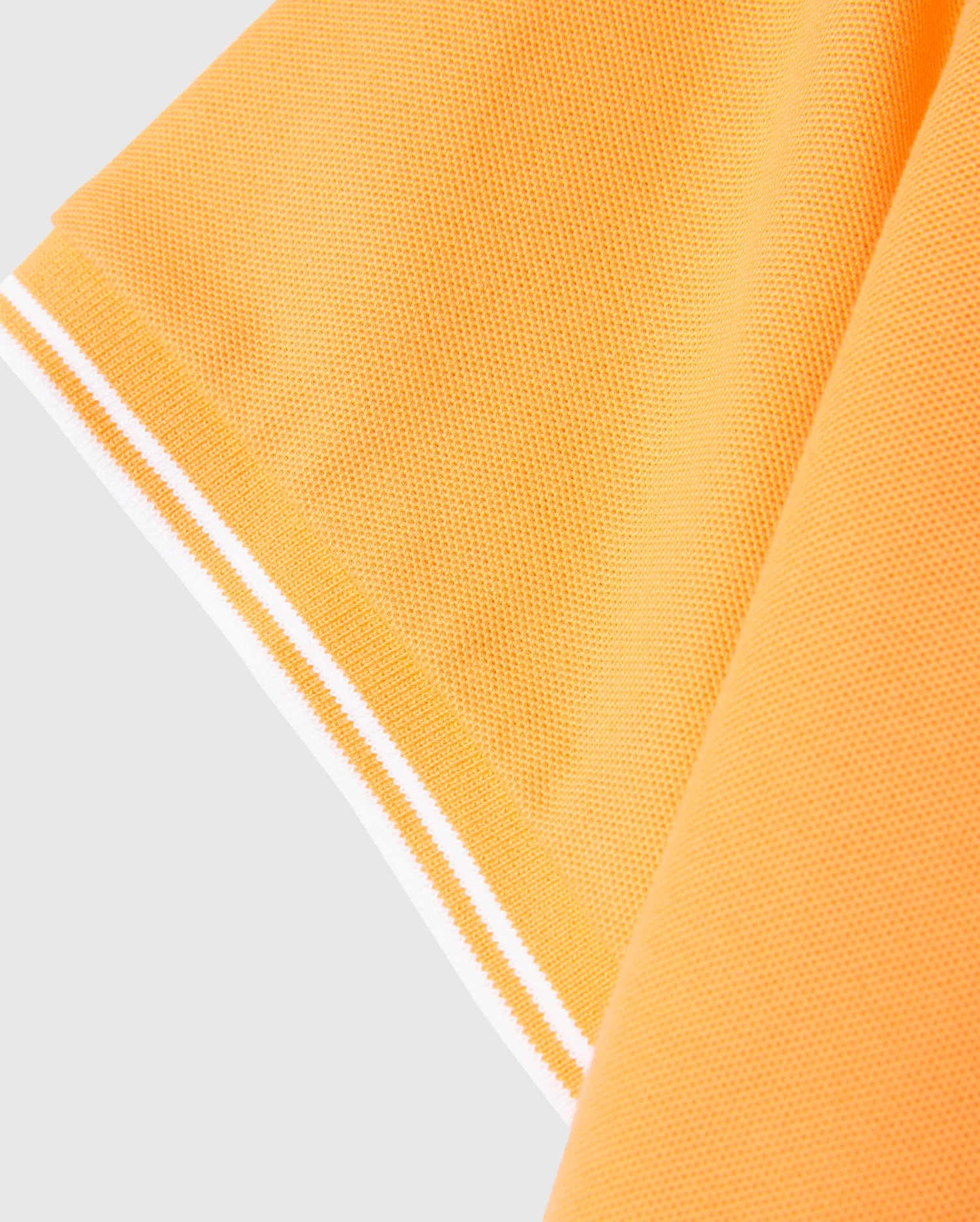 Close-up of the sleeve of an orange Psycho Bunny MENS BELTON PIQUE POLO - B6K575C200 with white stripes at the edge. The texture of the Pima cotton fabric is clearly visible, showcasing a fine knit pattern. The image focuses on the sleeve's hem and part of the shirt's main body, subtly highlighting the embroidered Bunny logo.