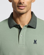 Wearing the Psycho Bunny Mens Jonas Stripe Collar Pique Polo, featuring a sage green micro-stripe design with a dark collar, crafted from soft Pima cotton. The shirt has a small bunny skull and crossbones logo on the left side. Image focuses on the upper body.