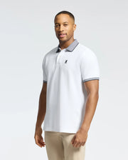 A man wears the Psycho Bunny MENS JONAS STRIPE COLLAR PIQUE POLO - B6K583F200, featuring a white micro-stripe design with gray collar and cuffs. His light pants complement the polo's small black emblem on the left, indicating its premium Pima cotton quality, as he looks neutrally at the camera.
