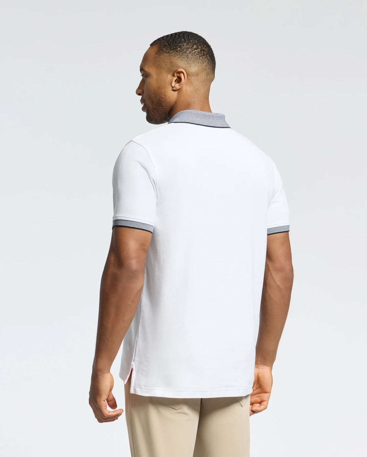A person is wearing the Psycho Bunny MENS JONAS STRIPE COLLAR PIQUE POLO (B6K583F200), a white Pima cotton shirt with gray collar and sleeve trim. They have short hair, beige pants, and are set against a plain white background, facing away.