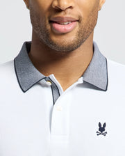 A person wears the MEN'S JONAS STRIPE COLLAR PIQUE POLO (B6K583F200) by Psycho Bunny, featuring white Pima cotton with a gray collar and an embroidered rabbit logo. The subtle micro-stripe texture enhances its elegance as the smiling individual showcases the shirt's exquisite detail.