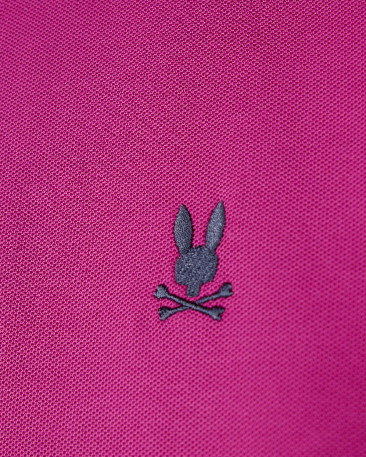 The men's Riviera Pique Polo Shirt from Psycho Bunny in pink Pima cotton showcases a dark gray embroidered Bunny appliqué with a rabbit head above two crossed bones.