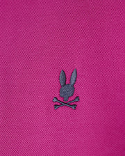 The men's Riviera Pique Polo Shirt from Psycho Bunny in pink Pima cotton showcases a dark gray embroidered Bunny appliqué with a rabbit head above two crossed bones.