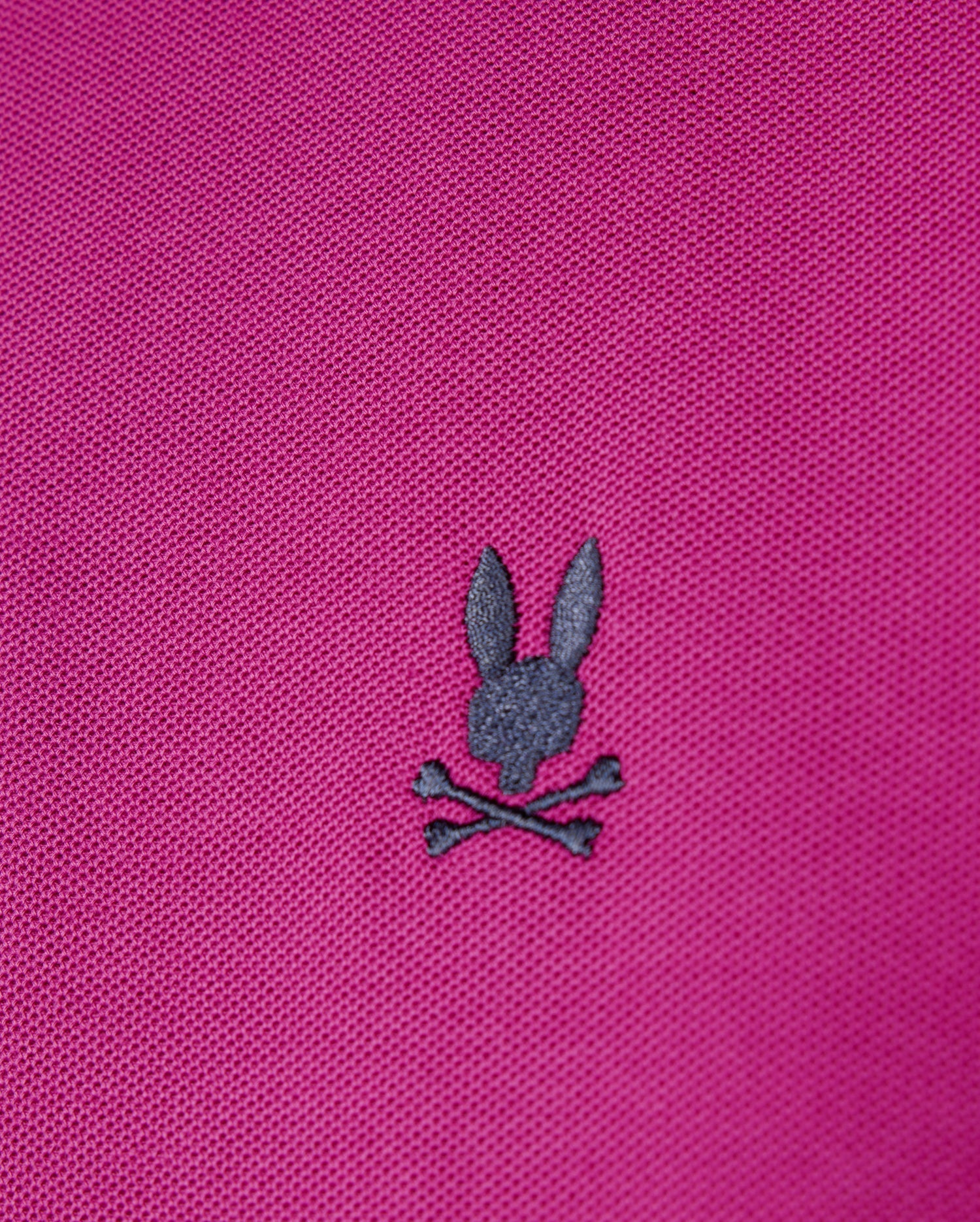 The men's Riviera Pique Polo Shirt from Psycho Bunny in pink Pima cotton showcases a dark gray embroidered Bunny appliqué with a rabbit head above two crossed bones.