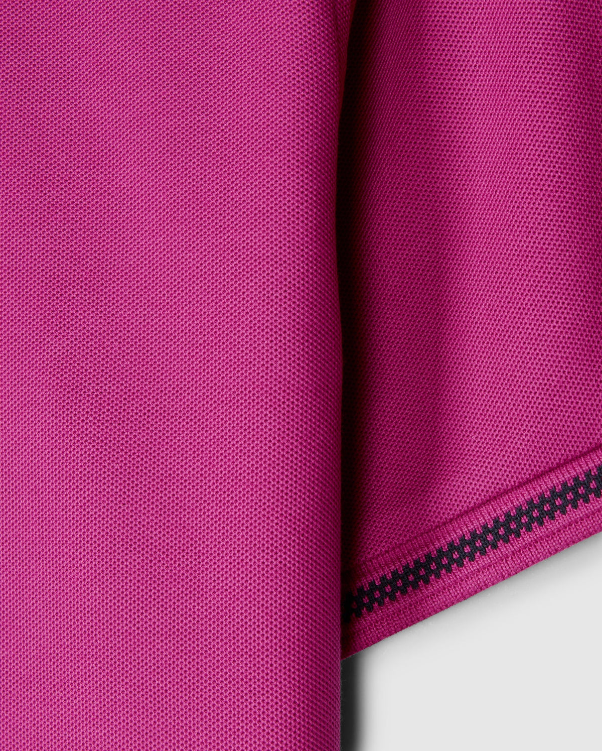 Close-up of the pink Pima cotton fabric from the Psycho Bunny MENS RIVIERA PIQUE POLO SHIRT - B6K640C200, showcasing a textured pattern with a folded edge on the right. A decorative black zigzag stitch enhances the edge, contrasting beautifully with the vibrant material, reminiscent of luxurious Riviera polo craftsmanship.