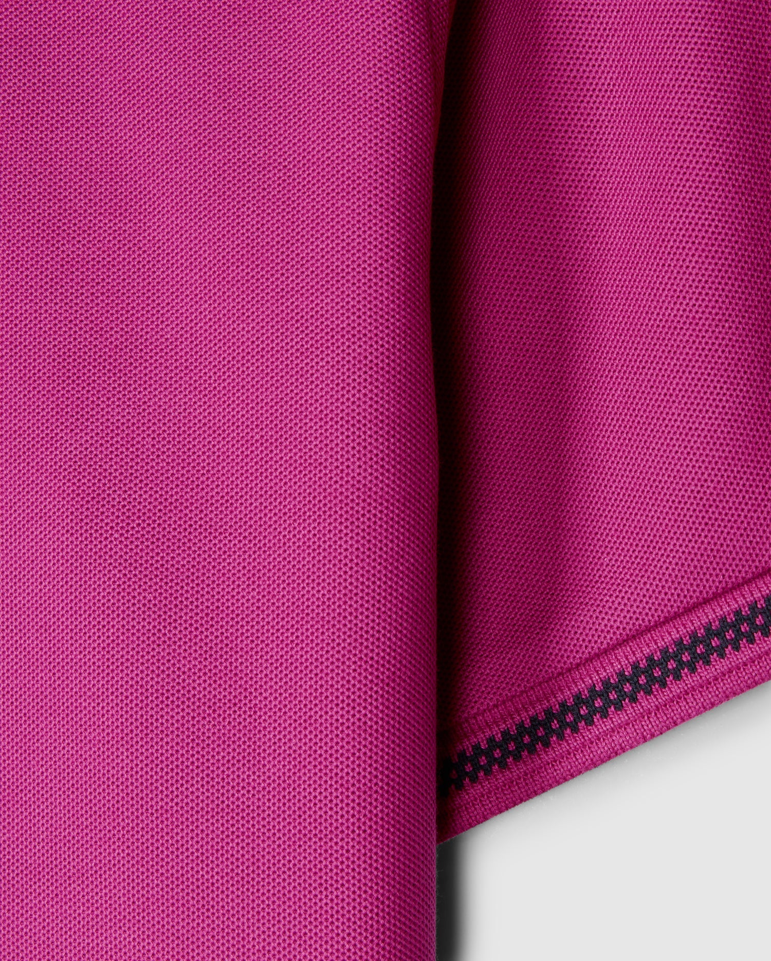 Close-up of the pink Pima cotton fabric from the Psycho Bunny MENS RIVIERA PIQUE POLO SHIRT - B6K640C200, showcasing a textured pattern with a folded edge on the right. A decorative black zigzag stitch enhances the edge, contrasting beautifully with the vibrant material, reminiscent of luxurious Riviera polo craftsmanship.