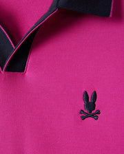 Close-up of a Psycho Bunny Men's Richards Johnny Collar Pique Polo Shirt in magenta, highlighting a solid pattern with a black collar and an embroidered bunny head with crossed bones on the chest. Crafted from breathable Pima cotton for ultimate comfort. Model number: B6K641C200.