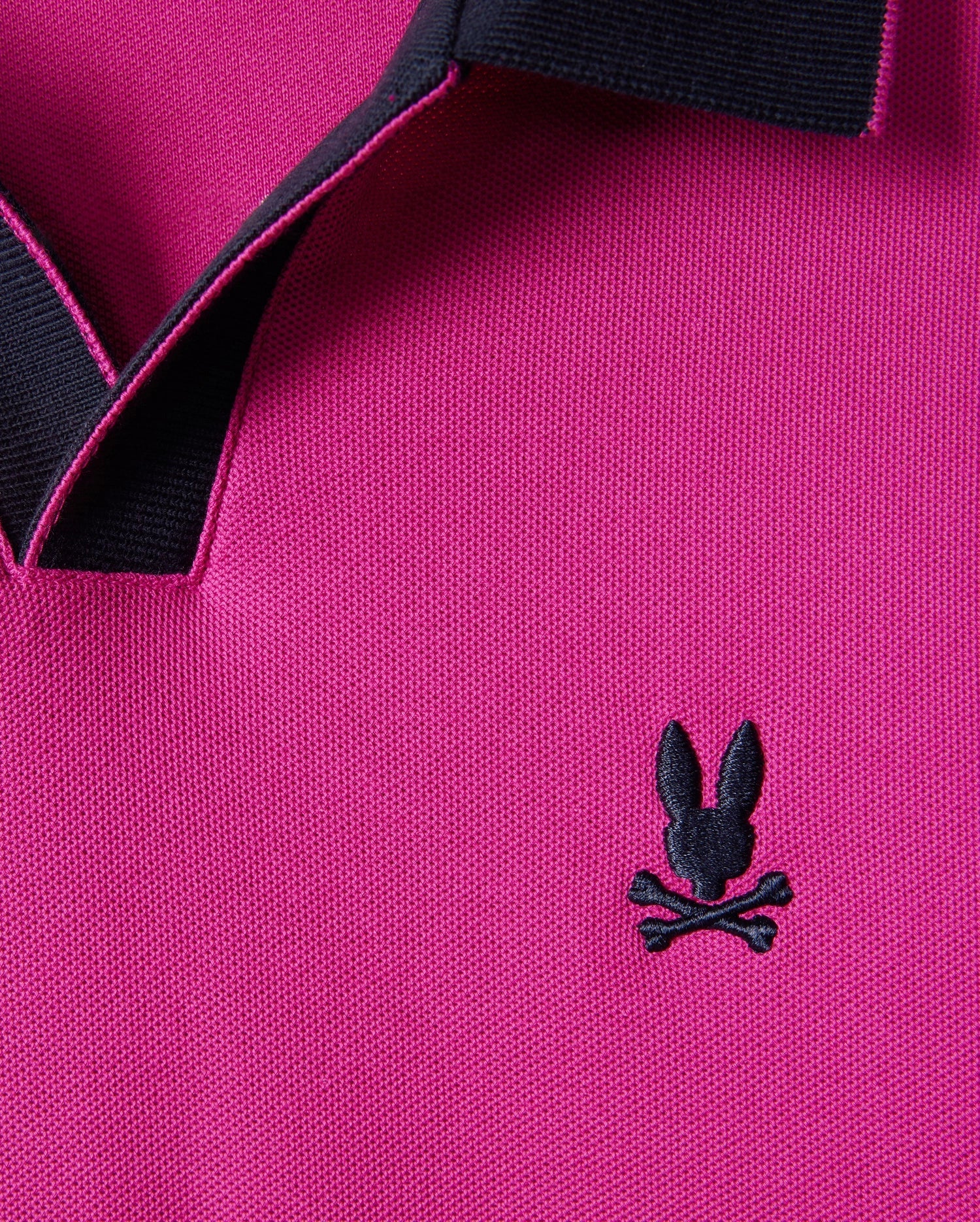 Close-up of a Psycho Bunny Men's Richards Johnny Collar Pique Polo Shirt in magenta, highlighting a solid pattern with a black collar and an embroidered bunny head with crossed bones on the chest. Crafted from breathable Pima cotton for ultimate comfort. Model number: B6K641C200.