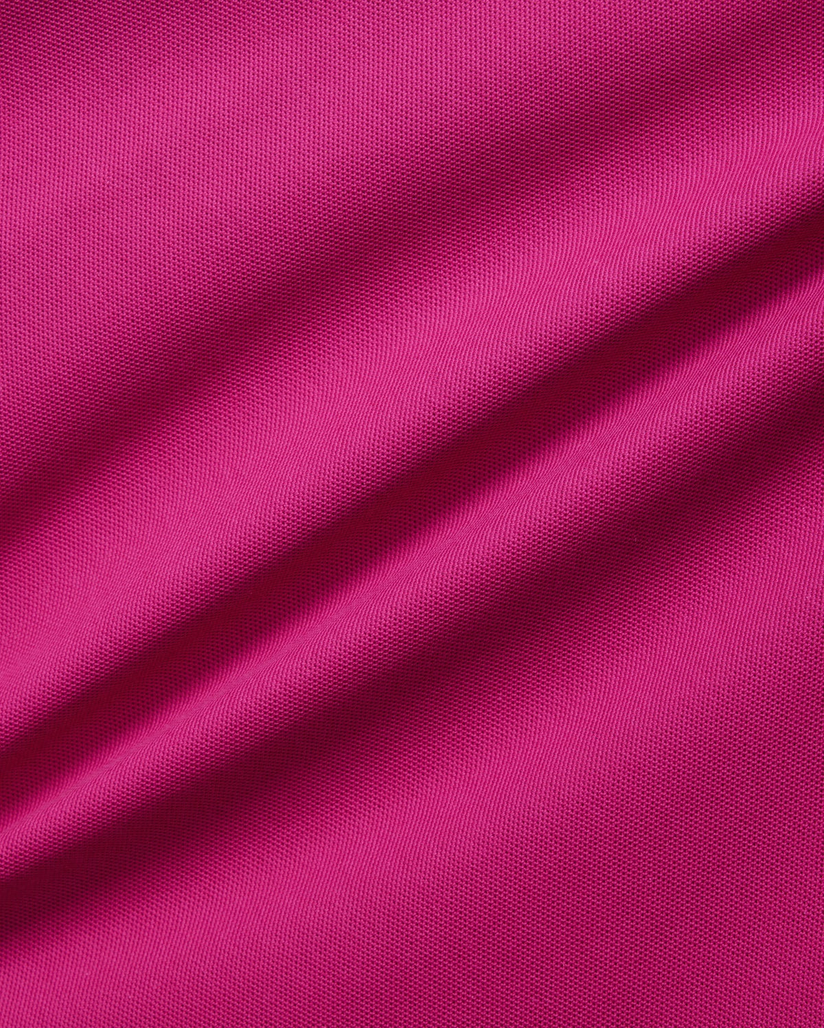 A close-up image of a vibrant pink, breathable Pima cotton fabric showcasing its texture. The material appears slightly wrinkled, with noticeable ripples running diagonally across the image, emphasizing the solid pattern's detail and quality in this Psycho Bunny Men's Richards Johnny Collar Pique Polo Shirt - B6K641C200.