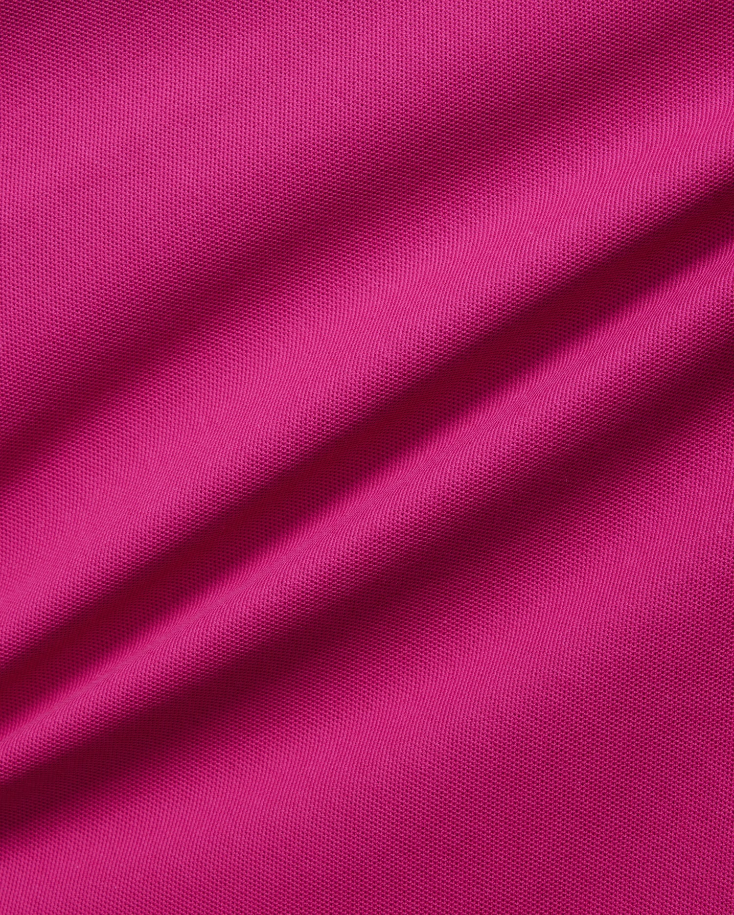 A close-up image of a vibrant pink, breathable Pima cotton fabric showcasing its texture. The material appears slightly wrinkled, with noticeable ripples running diagonally across the image, emphasizing the solid pattern's detail and quality in this Psycho Bunny Men's Richards Johnny Collar Pique Polo Shirt - B6K641C200.