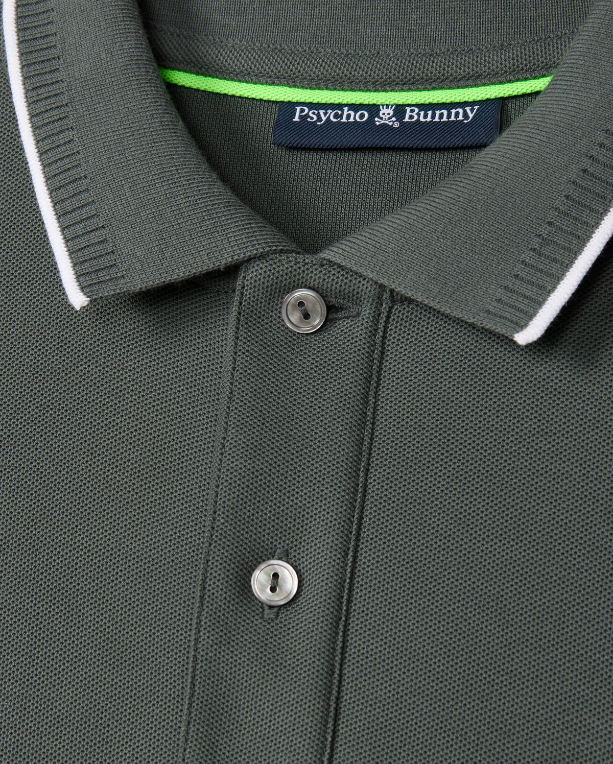 Close-up image of the Psycho Bunny Men's Kingston Pique Polo Shirt (B6K764D200) in vibrant green, crafted from Pima cotton with a ribbed collar and two buttons. The collar features a thin white trim, while an embroidered Bunny patch on the label inside reads "Psycho Bunny" with a logo of a bunny above the text.