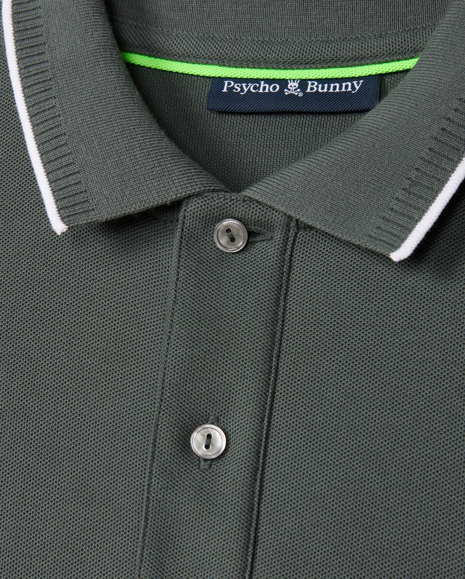 Close-up image of the Psycho Bunny Men's Kingston Pique Polo Shirt (B6K764D200) in vibrant green, crafted from Pima cotton with a ribbed collar and two buttons. The collar features a thin white trim, while an embroidered Bunny patch on the label inside reads "Psycho Bunny" with a logo of a bunny above the text.