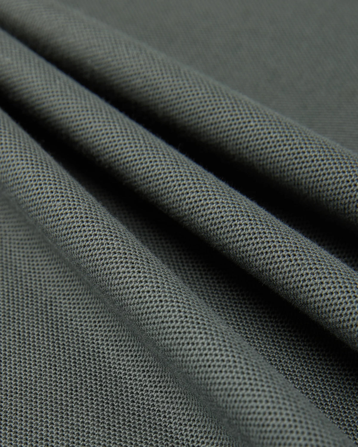 A close-up view of smooth, dark green Pima cotton with a fine, textured weave. The fabric is draped, creating gentle folds and shadows that highlight its soft and flexible nature, reminiscent of a luxurious Psycho Bunny MENS KINGSTON PIQUE POLO SHIRT - B6K764D200.