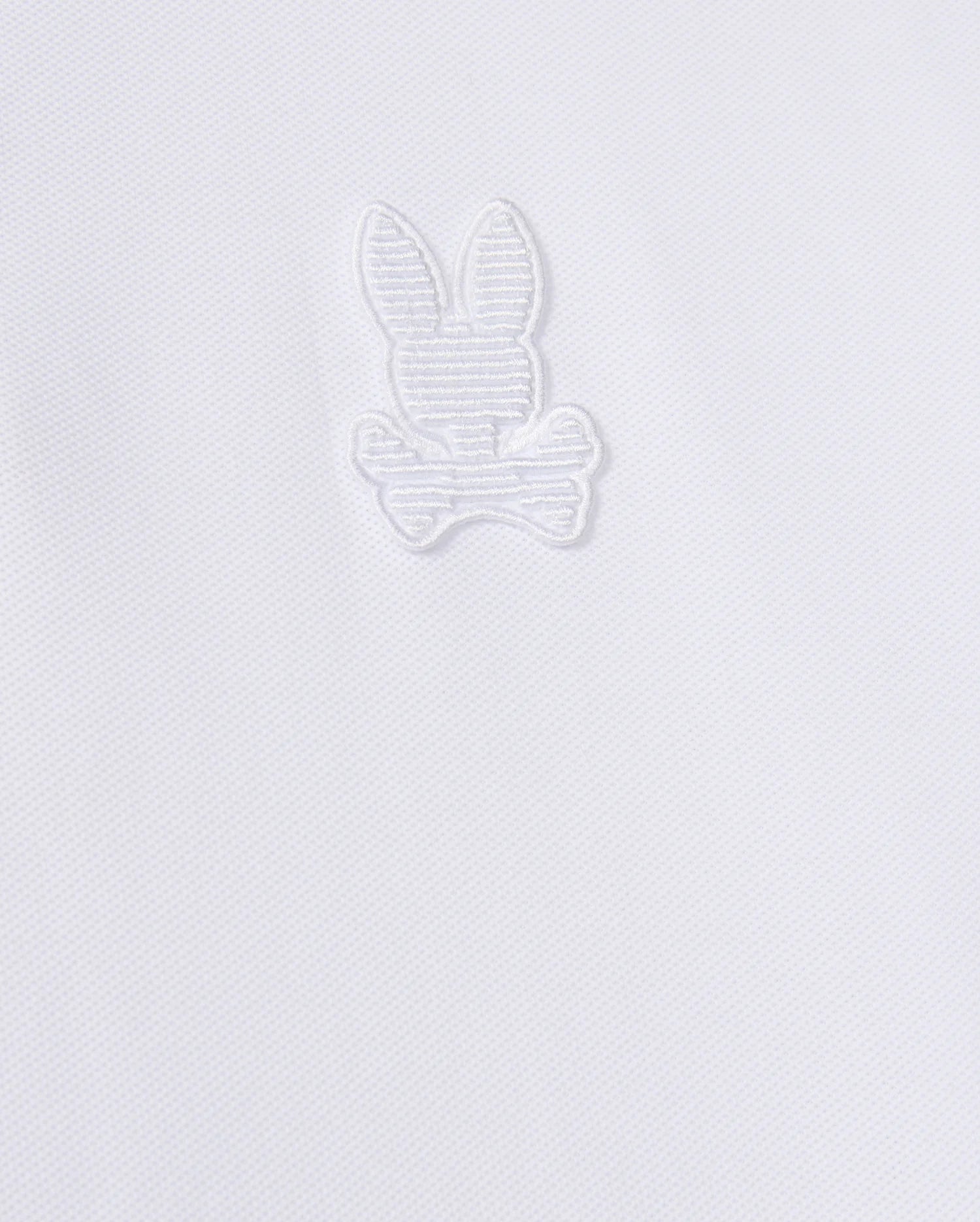 The Psycho Bunny MENS KINGSTON PIQUE POLO SHIRT - B6K764D200 is crafted from soft Pima cotton and features an embroidered Bunny patch with long ears, sitting above a pair of crossed bones. The design is stitched in matching white thread, blending subtly with the fabric.