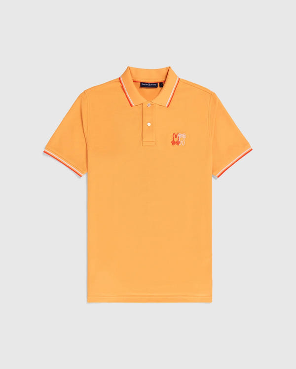 A bright orange Psycho Bunny MENS WINTON PIQUE POLO SHIRT - B6K841A2PC with a collar and short sleeves. Crafted from luxurious Peruvian Pima cotton in a diamond-knit piqué, it features red and white stripes on the collar and sleeve cuffs. An embroidered patch with a colorful cartoon character is visible on the left chest area.