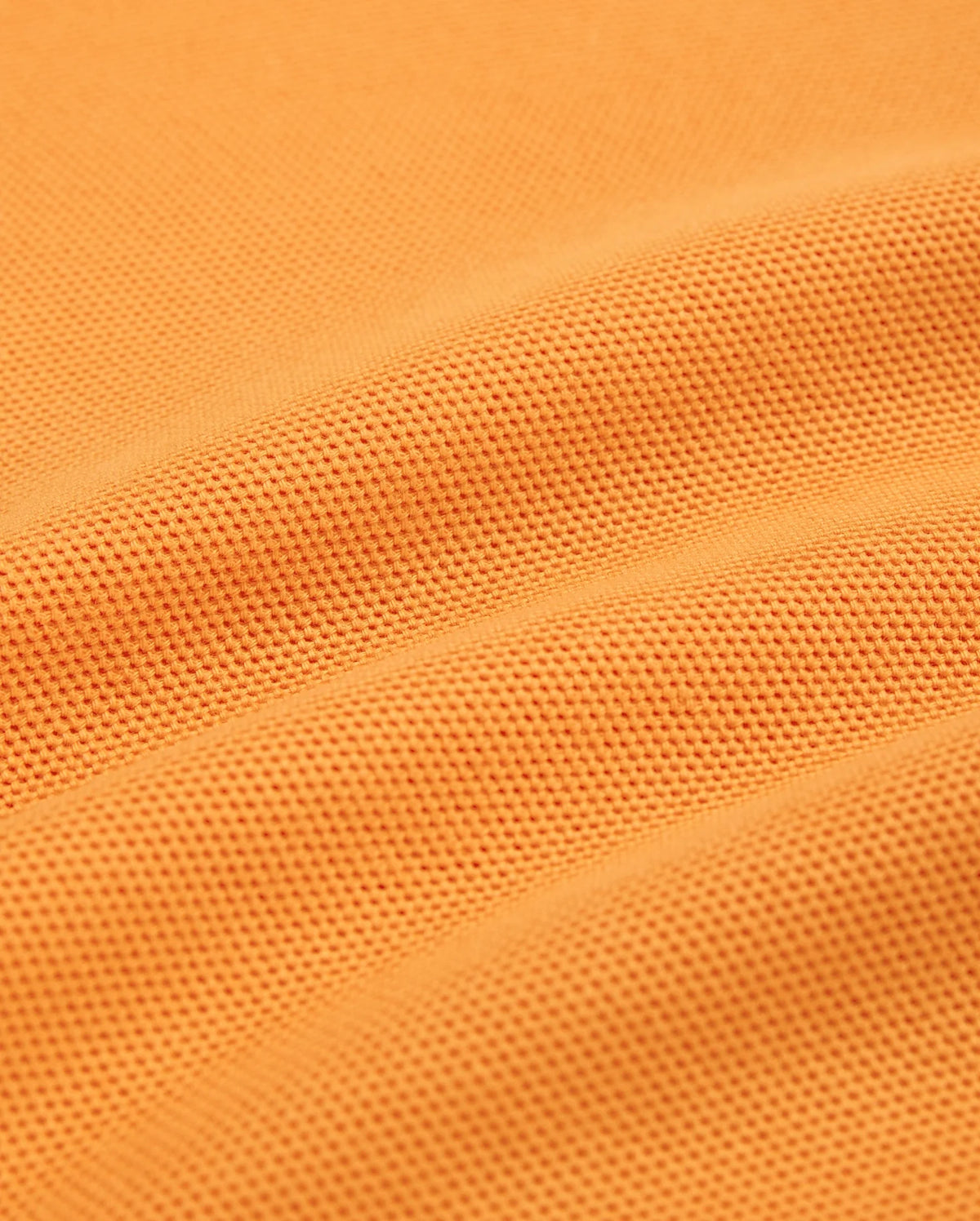 Close-up of a textured orange fabric with small, dotted patterns. The fabric, resembling Peruvian Pima cotton used in Psycho Bunny's MENS WINTON PIQUE POLO SHIRT - B6K841A2PC, appears to be slightly folded, creating gentle, curved lines and shadows across the surface.