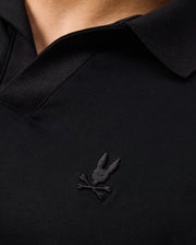 Close-up of a black MENS BROADWAY PIMA INTERLOCK JOHNNY COLLAR POLO by Psycho Bunny, crafted from durable lustre mercerized Pima cotton and featuring a stitched logo with a rabbit head above crossed bones. The shirt's collar and part of the neckline are visible.