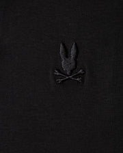 The Psycho Bunny MENS BROADWAY PIMA INTERLOCK JOHNNY COLLAR POLO - B6K891D200 is a black fabric polo made from durable lustre Mercerized Pima cotton. It features a subtle embroidered design of a stylized rabbit head above two crossed bones, evoking the classic skull and crossbones motif.