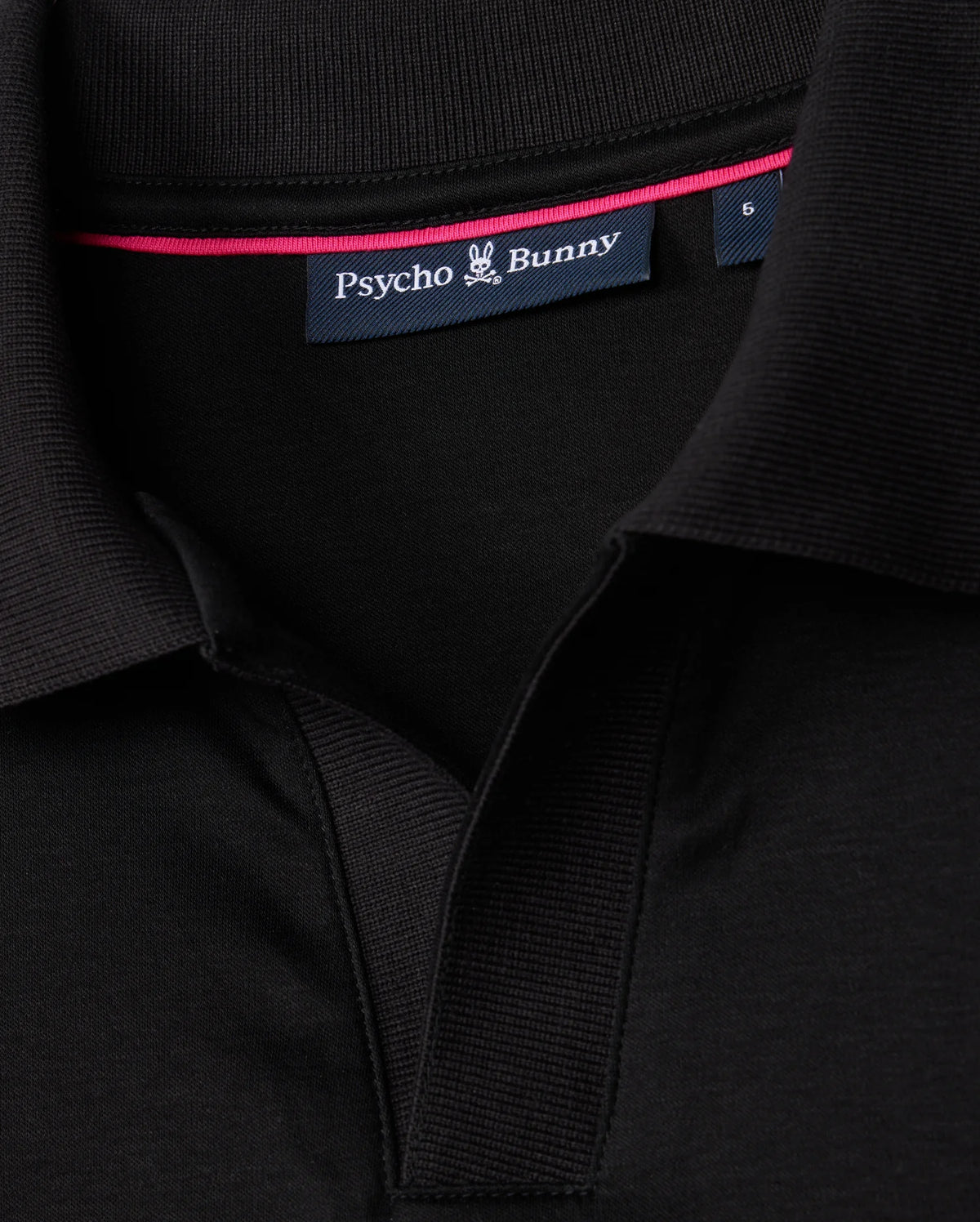Detailed view of the collar on the MENS BROADWAY PIMA INTERLOCK JOHNNY COLLAR POLO by Psycho Bunny, crafted from durable mercerized Pima cotton. The black shirt displays a visible "Psycho Bunny" label and a small stylized bunny logo, with a pink trim on the inner collar for an added touch of flair.