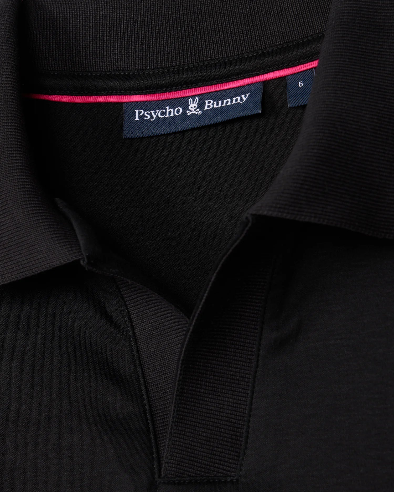 Detailed view of the collar on the MENS BROADWAY PIMA INTERLOCK JOHNNY COLLAR POLO by Psycho Bunny, crafted from durable mercerized Pima cotton. The black shirt displays a visible "Psycho Bunny" label and a small stylized bunny logo, with a pink trim on the inner collar for an added touch of flair.